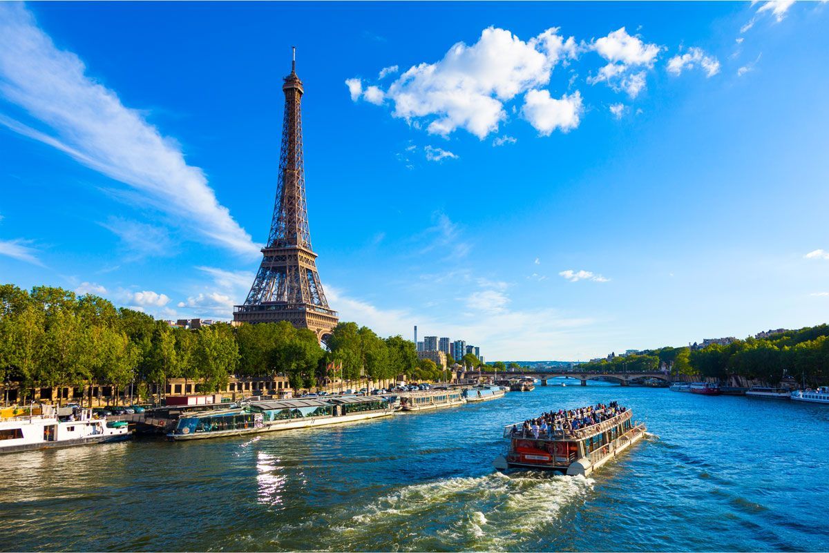 La Torre Eiffel en París, Francia, se eleva sobre el río Sena con un barco navegando en un día soleado.
