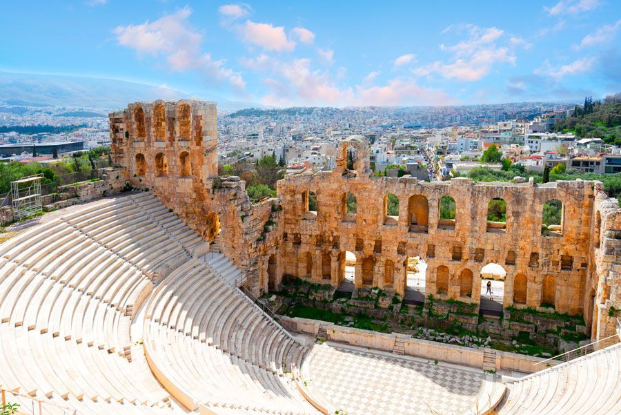 Ruinas del Odeón de Herodes Ático, un antiguo teatro en Atenas, Grecia, con asientos de piedra y arcos con la ciudad como telón de fondo.