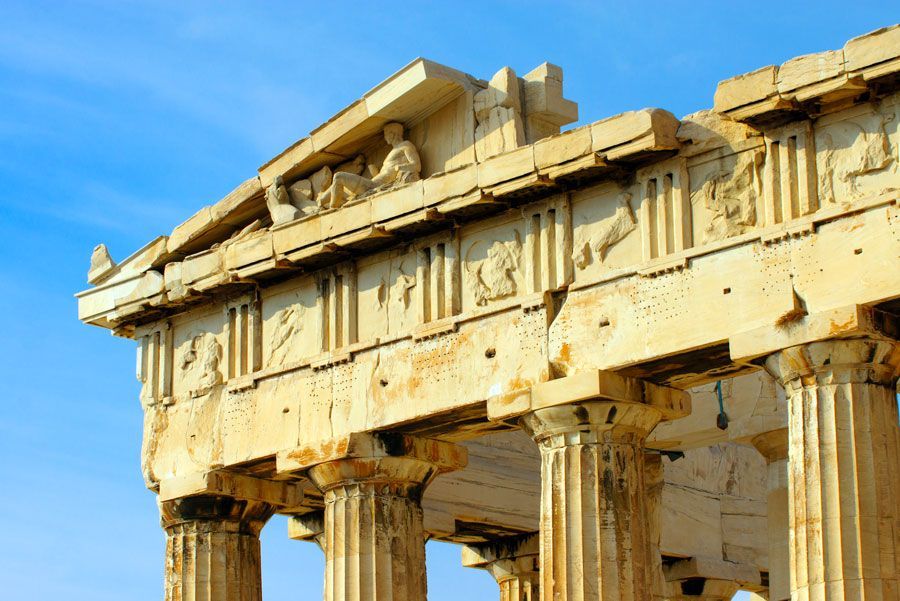 La sección superior del Partenón en Atenas, Grecia, muestra columnas dóricas y esculturas detalladas en el friso contra un cielo azul brillante.