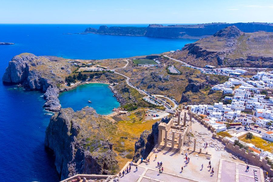 Vista aérea de Lindos, Rodas, Grecia, con la Acrópolis en una colina con vistas al mar azul y edificios blancos.