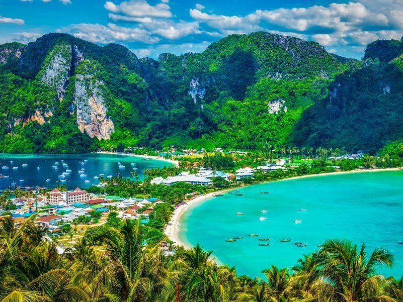 Vista aérea panorámica de la isla Phi Phi, Tailandia, con exuberantes montañas verdes, aguas turquesas y una playa curva.