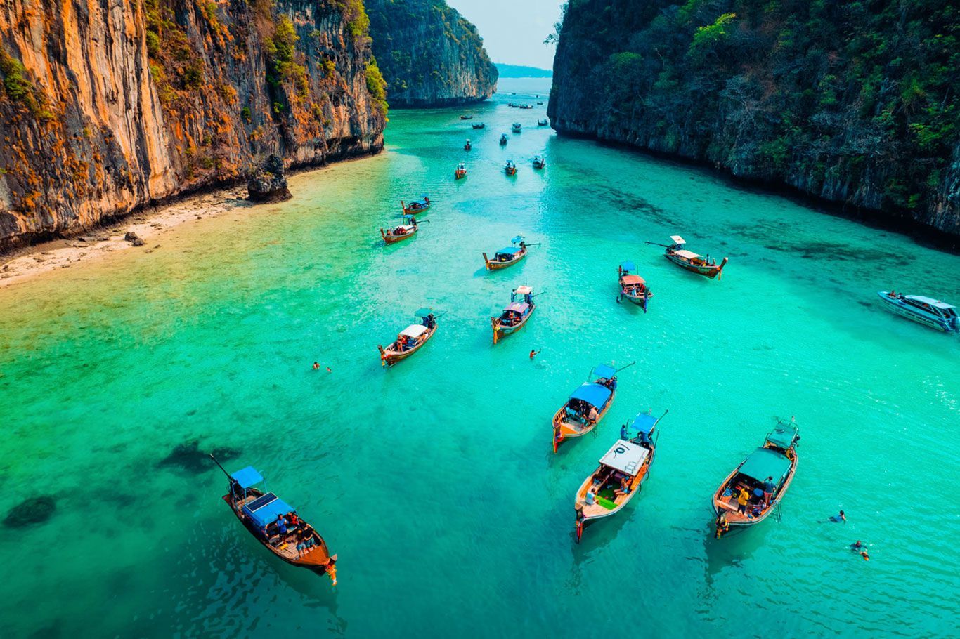Barcos en una bahía turquesa rodeada de acantilados. Paisaje tropical con aguas cristalinas y varias lanchas de cola larga.