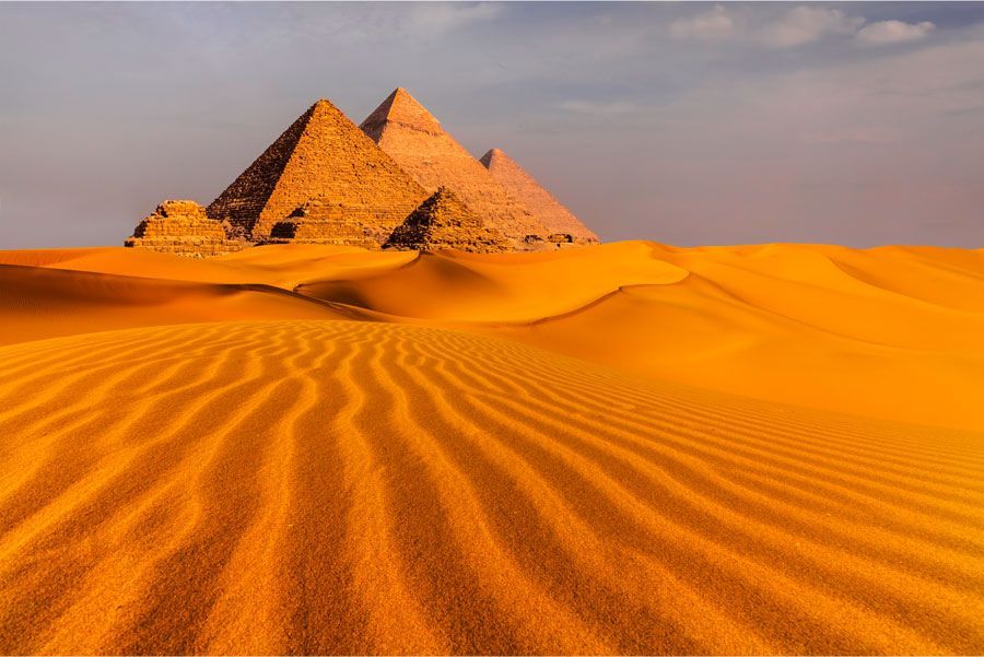 Las pirámides de Giza, Egipto, se elevan sobre las dunas de arena dorada bajo un cielo despejado, bañadas por la cálida luz del sol.