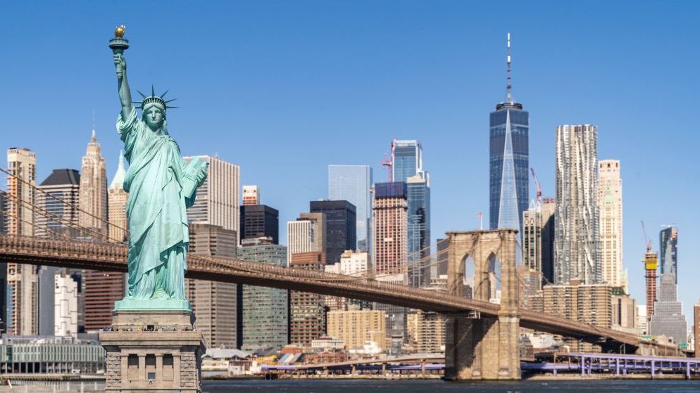 La Estatua de la Libertad, el Puente de Brooklyn y el horizonte de Manhattan en un día soleado. Los famosos monumentos se recortan contra un cielo azul despejado.