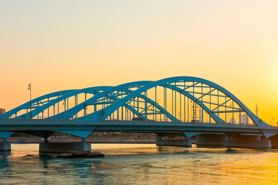 Puente azul arqueado sobre el agua contra un cielo al atardecer en Abu Dhabi.