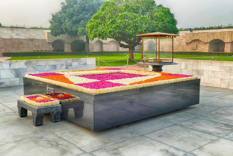 Tumba de Mahatma Gandhi en el Raj Ghat de Delhi. Una plataforma rectangular de piedra negra cubierta de flores, con una pequeña mesa de piedra al frente.