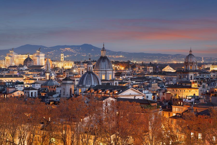 Paisaje urbano de Roma al anochecer, mostrando edificios con cúpulas y agujas bajo un cielo colorido.