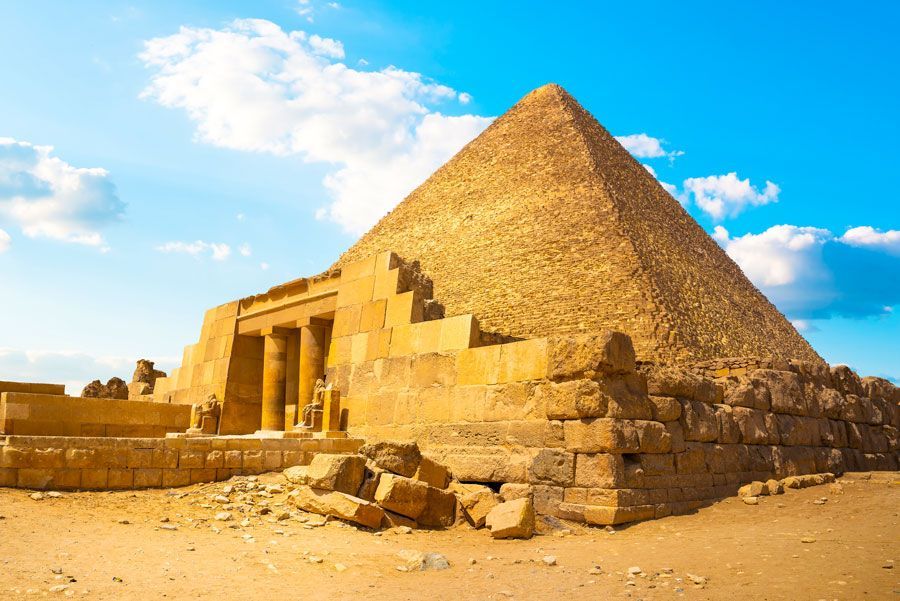 Pirámide de Giza, Egipto, que se yergue en el desierto bajo un cielo azul. Estructura de entrada y escombros en primer plano.