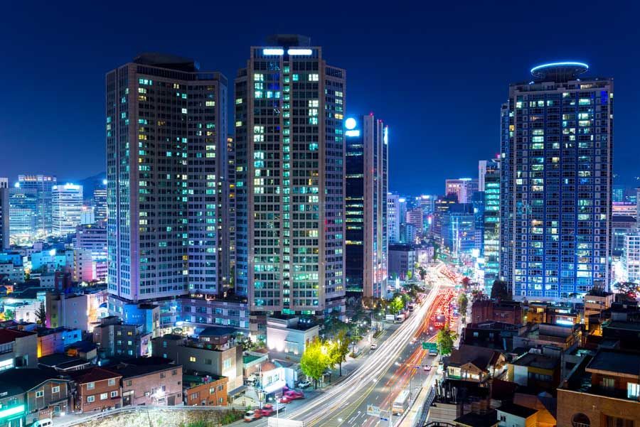 Horizonte de la ciudad por la noche, altos edificios iluminados dominan, carretera con estelas de luz de automóviles, cielo azul.