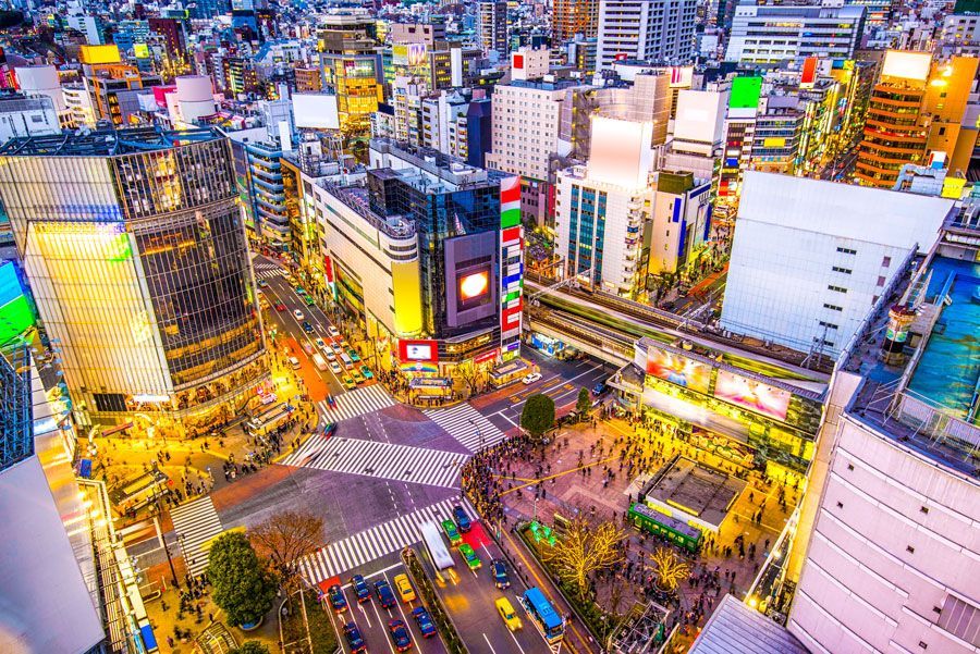 Vista aérea del cruce de Shibuya, Tokio, iluminado con luces brillantes al anochecer. La gente cruza la calle en múltiples direcciones.