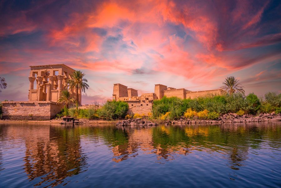 Las ruinas del antiguo Egipto en la orilla de un río se reflejan en el agua bajo un espectacular cielo al atardecer.