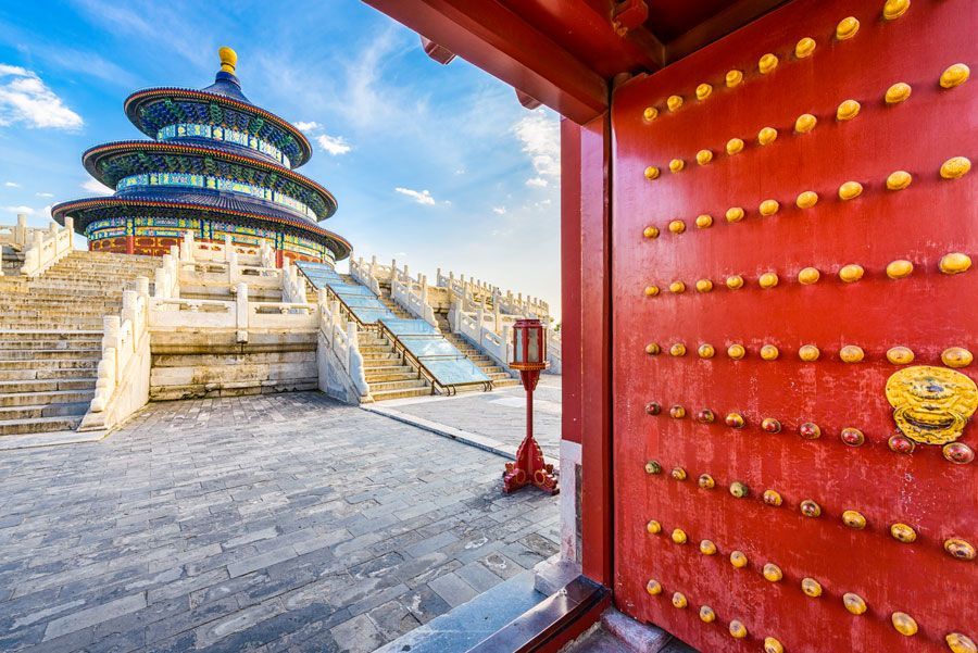 Templo del Cielo, Pekín, China. Las puertas rojas se abren para revelar el templo de varios niveles, con techo azul y escalones blancos bajo un cielo azul.