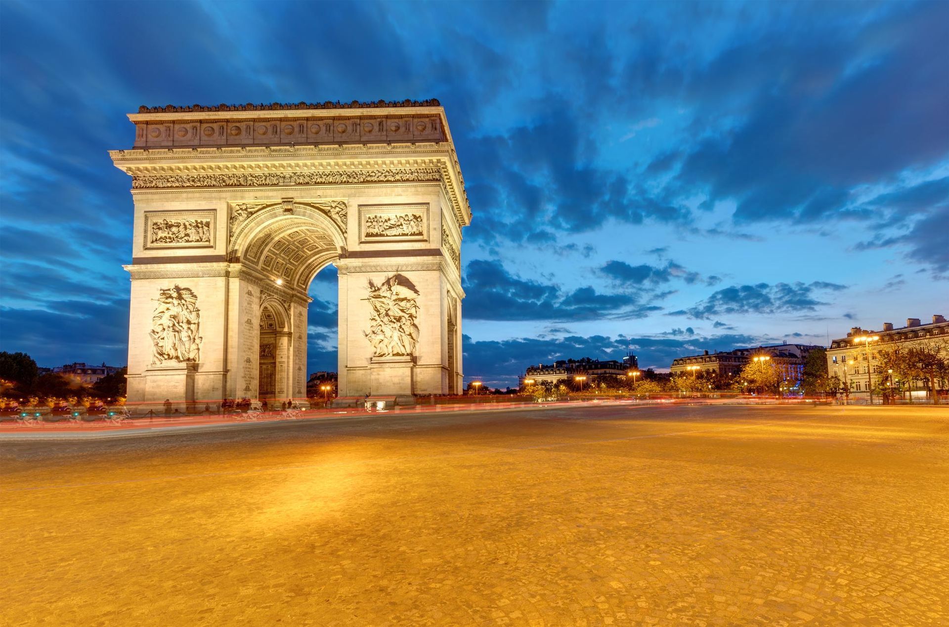 Arco del Triunfo en París al anochecer, iluminado contra un cielo crepuscular.