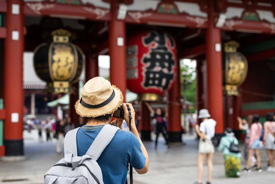 Una persona con un sombrero de paja fotografía un templo en Japón, con una gran linterna roja en el fondo.