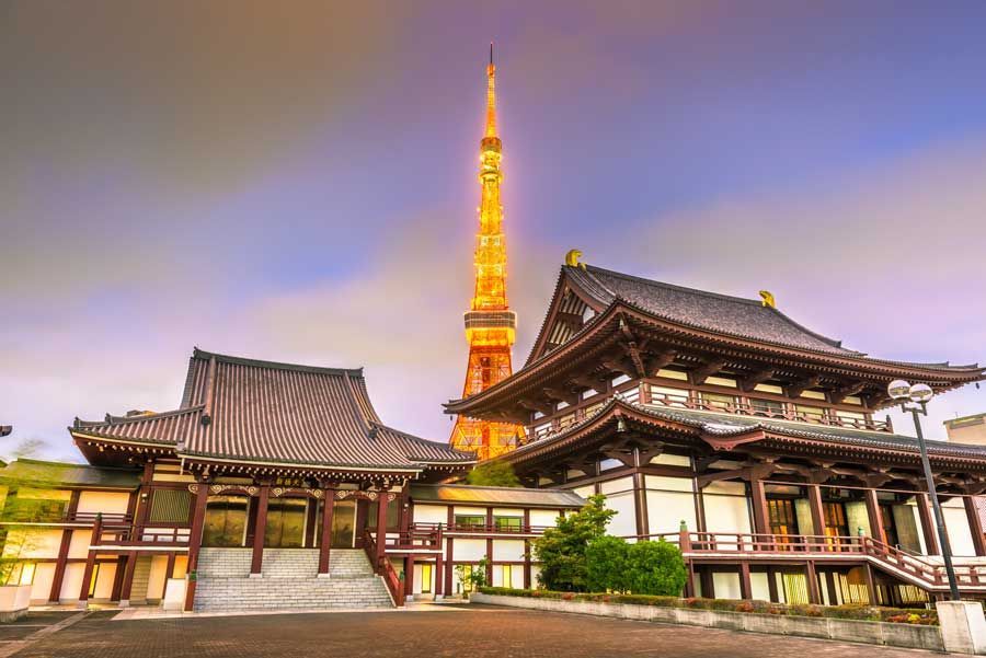 Edificios de templos japoneses con una Torre de Tokio iluminada al fondo al anochecer.