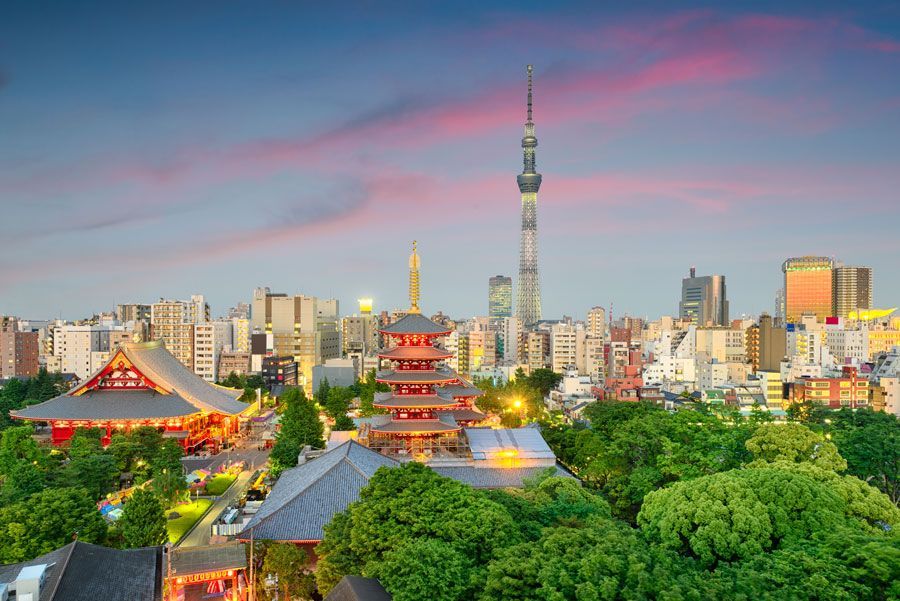 El horizonte de Tokio con templos rojos en primer plano, exuberantes árboles verdes y la torre Tokyo Skytree bajo un atardecer rosa y azul.