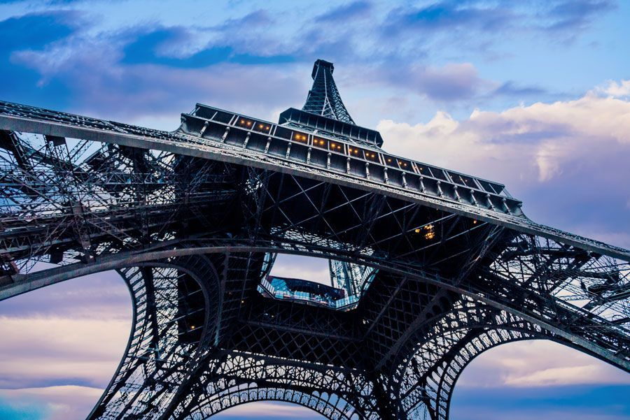 Torre Eiffel en París, Francia, vista desde abajo contra un cielo azul nublado, con una intrincada estructura de celosía de hierro.