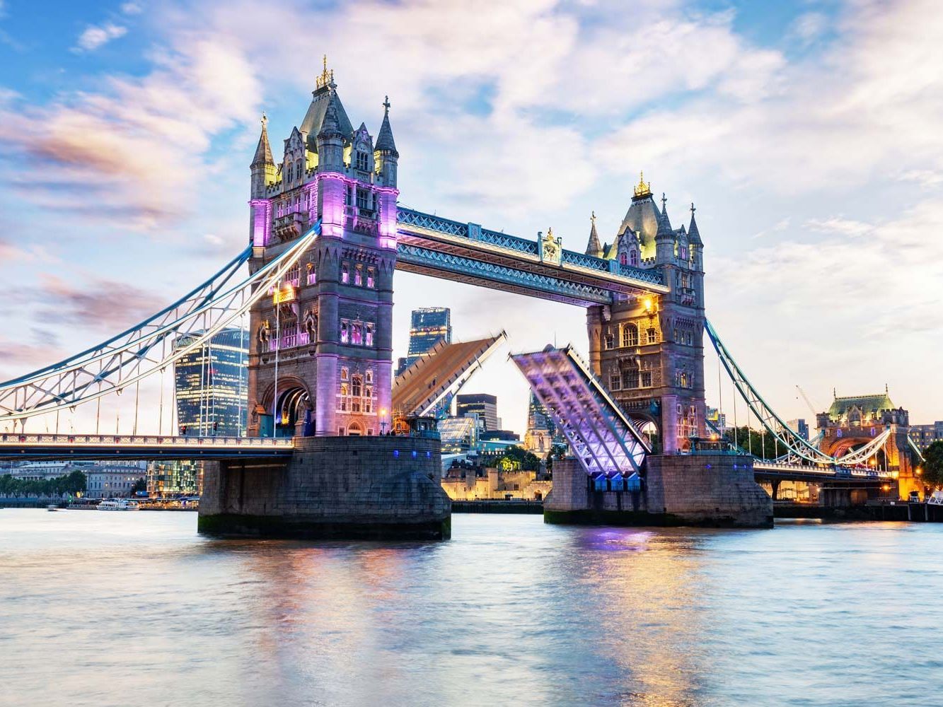 Tower Bridge, Londres, iluminado al atardecer con el puente levadizo abierto, mostrando el río y el horizonte de la ciudad.