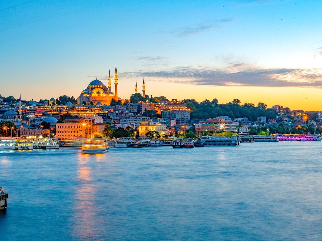 Vista de Estambul, Turquía, al anochecer. El paisaje urbano destaca por sus edificios iluminados y la Mezquita de Süleymaniye, reflejada en el estrecho del Bósforo.