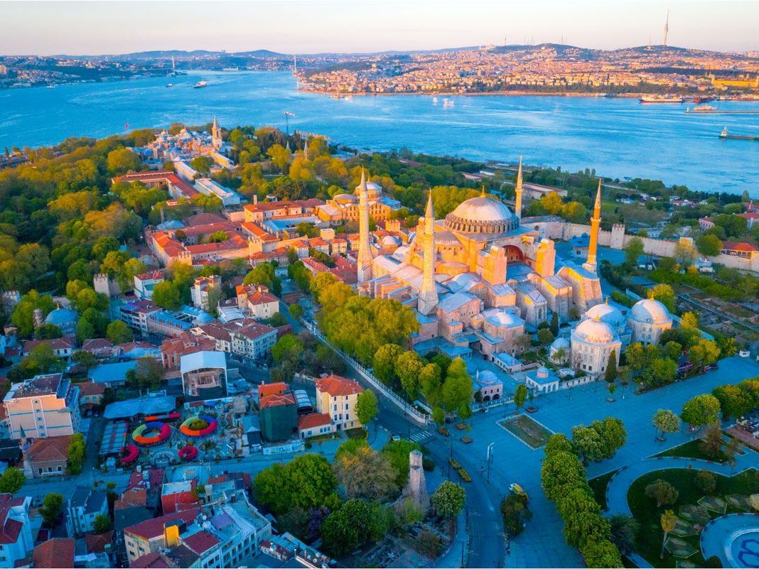 Vista aérea de Estambul, Turquía, con Santa Sofía en un lugar destacado. Edificios y árboles rodean la mezquita, con un estrecho azul al fondo.