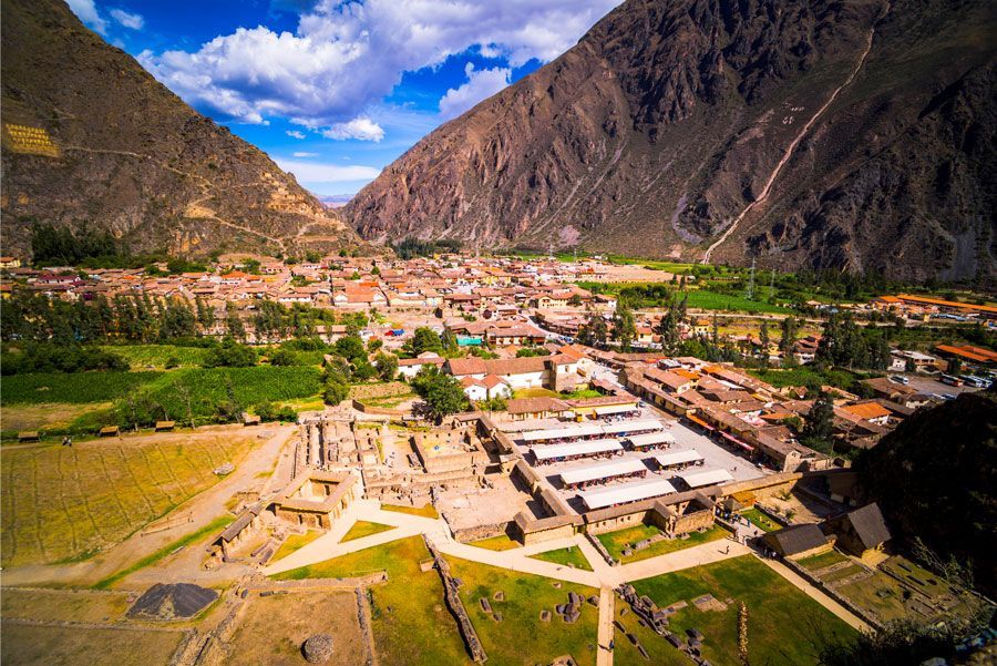 Ollantaytambo, Perú, vista aérea: ruinas incas en primer plano con la ciudad y las montañas al fondo.