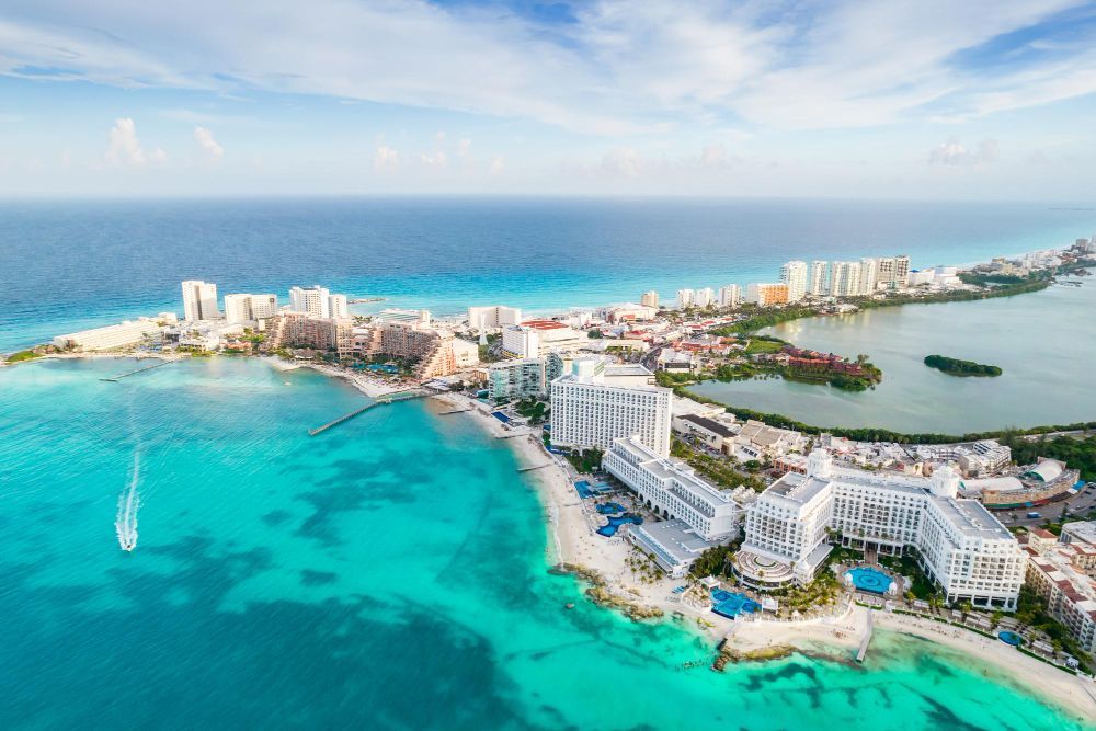 Vista aérea de Cancún, México. El océano turquesa rodea una península rodeada de hoteles y playas bajo un cielo azul.