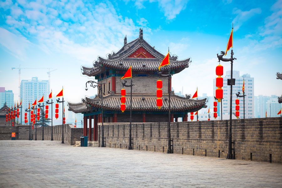Fortaleza de piedra en Xi'an, China, con una torre de pagoda tradicional y banderas rojas y linternas contra un cielo azul.