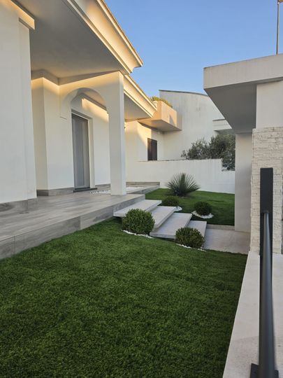 Piccolo giardino interno con giovani alberi, terreno sabbioso e edifici bianchi tutt'intorno.