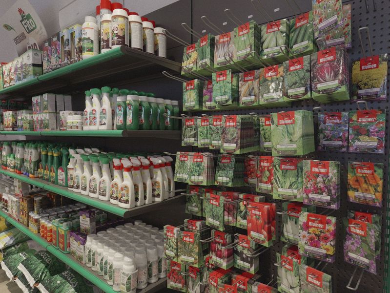 Scaffali pieni di prodotti da giardinaggio e bustine di semi in una corsia di un negozio.