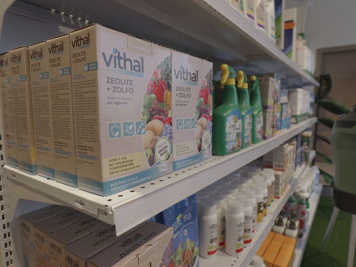 Scaffale di prodotti per la pulizia della casa e scatole di Vithal in una corsia di un negozio, con flaconi verdi e contenitori bianchi.