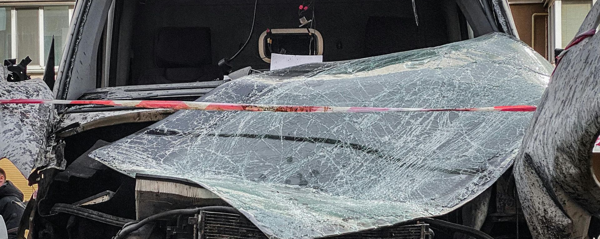Severely damaged vehicle with shattered windshield, crushed front end, and major structural impact from collision.