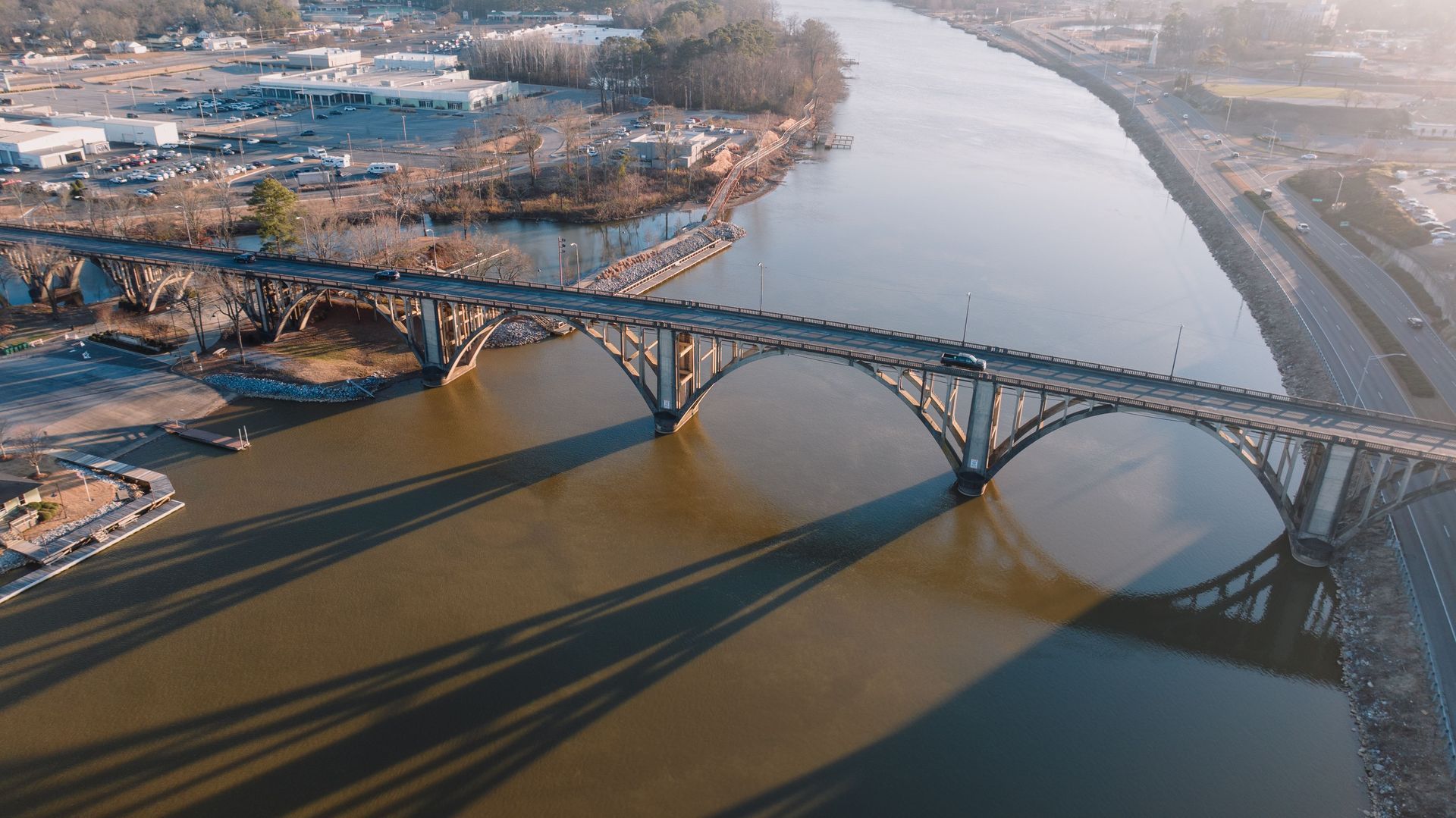 Professional aerial drone view of the historic concrete arch Broad Street Bridge crossing the Coosa River in Gadsden, Alabama during sunset.
