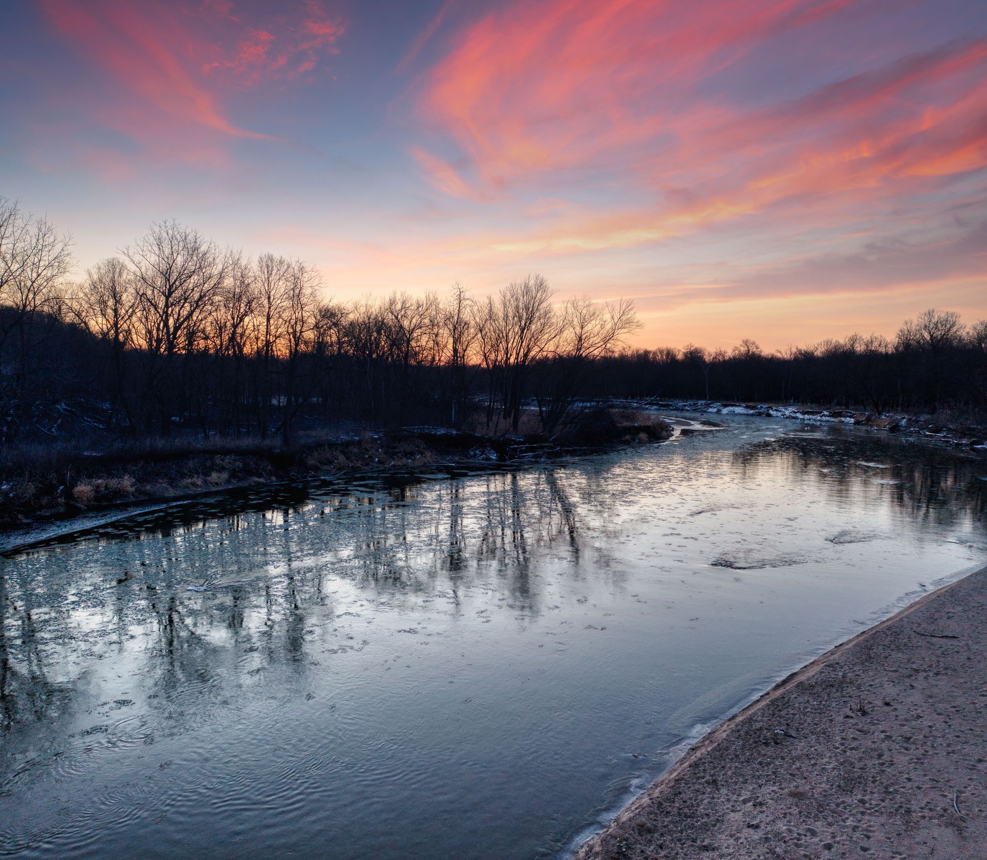 A colorful winter sunset reflecting off the partially frozen water of the Mississippi River in Elk River, Minnesota