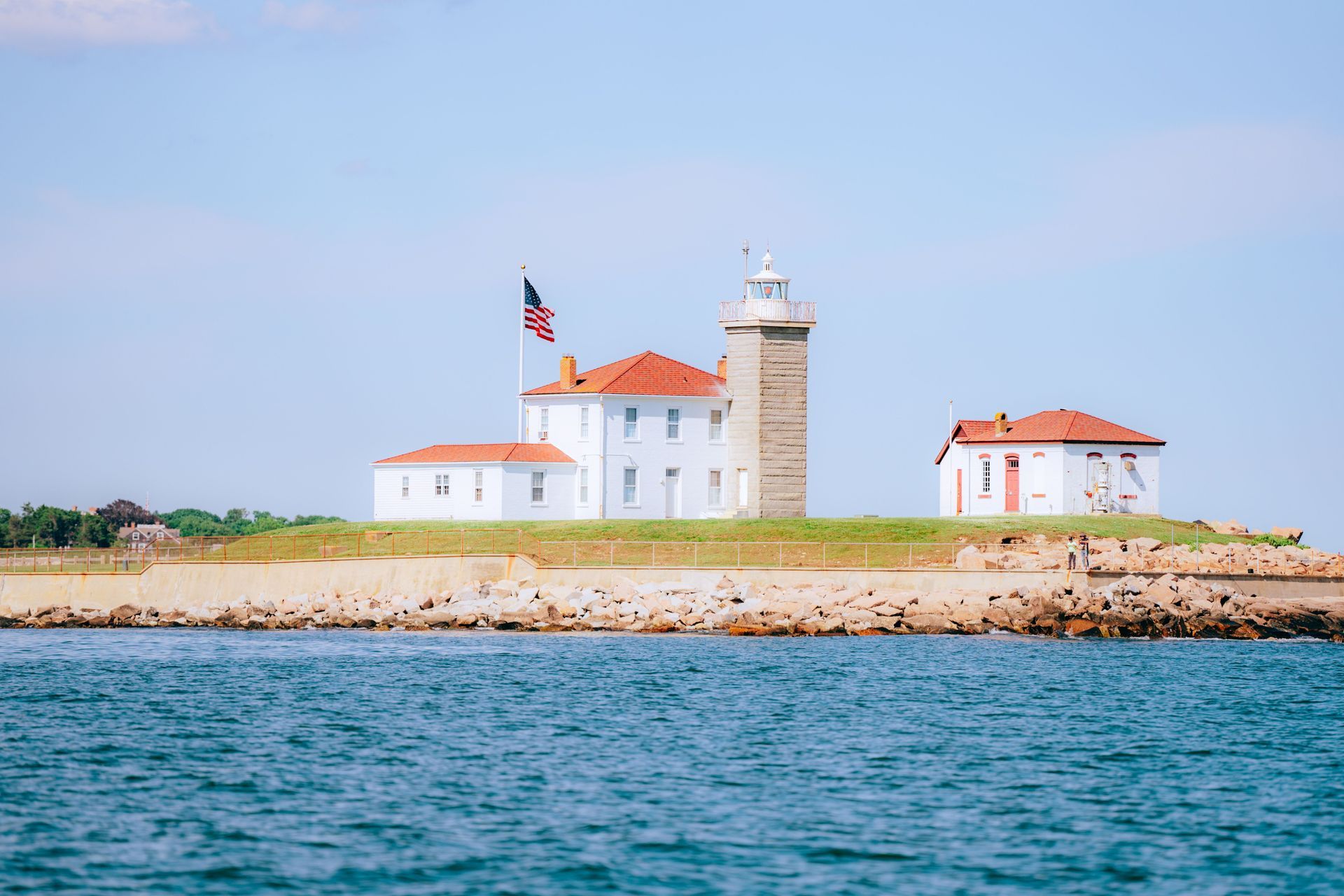 The Watch Hill Lighthouse and ocean shore under a blue sky in Westerly, Rhode Island. 