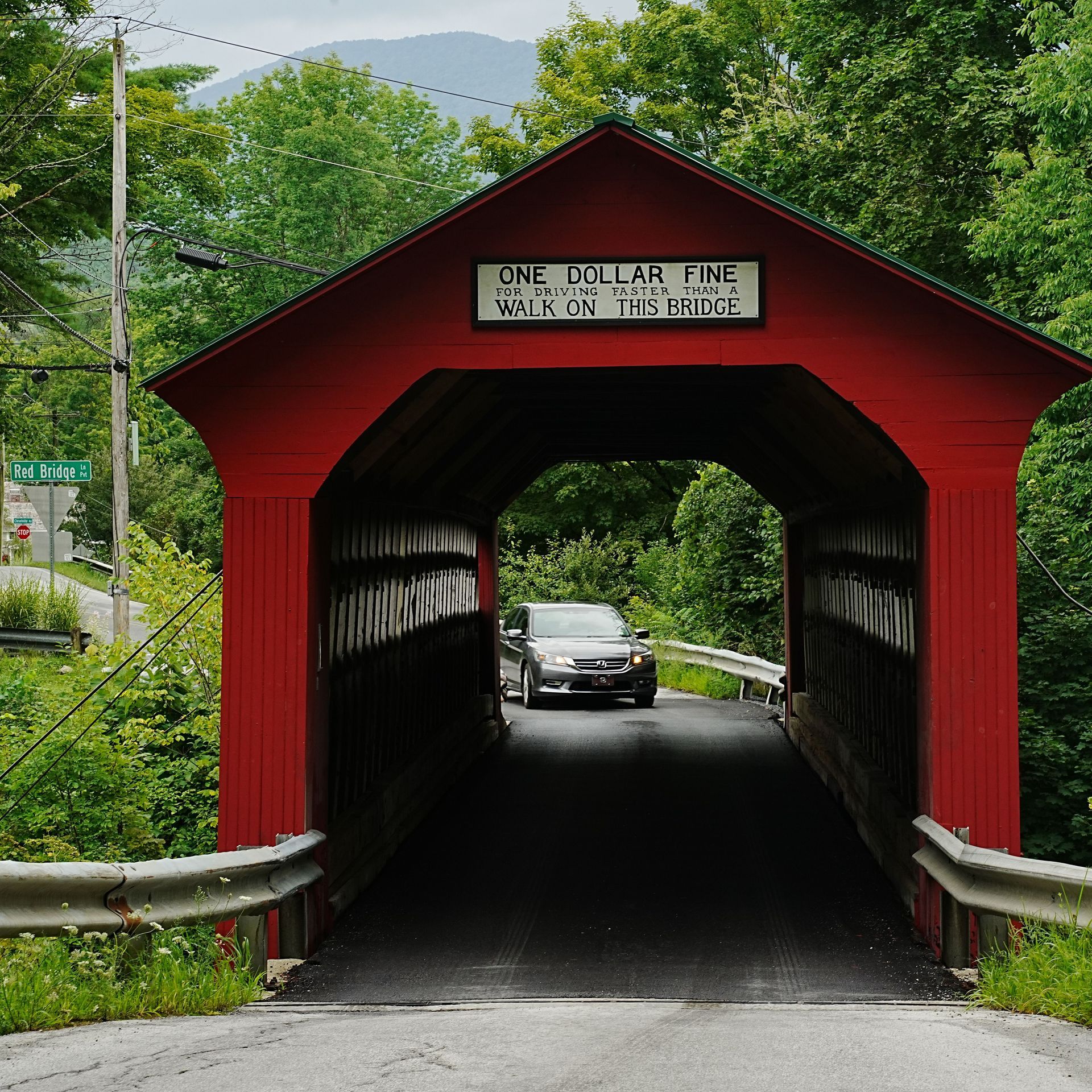 A gray sedan driving through the red historic Chiselville Covered Bridge in Sunderland, Vermont