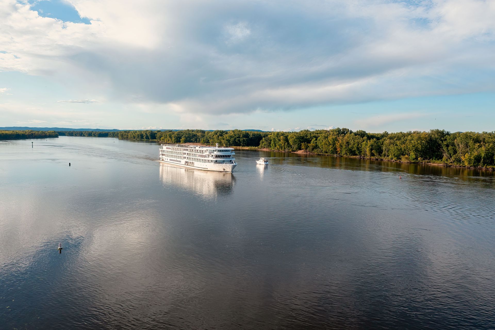 A modern white luxury cruise ship navigating the calm waters of the Mississippi River.