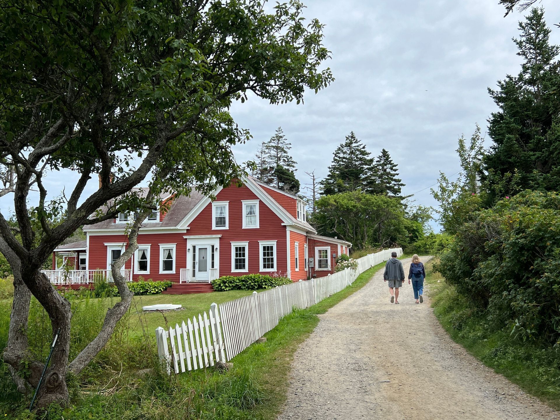 People walking on a dirt road past a historic red cottage on Monhegan Island, Maine