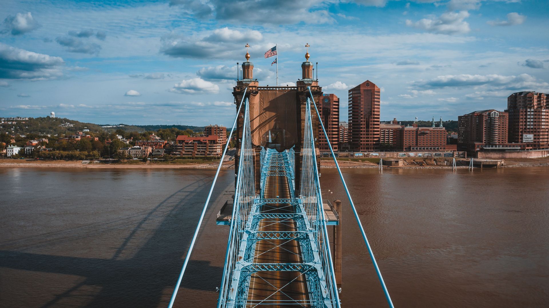 Symmetry view looking down the blue steel deck of the historic Roebling Suspension Bridge over the river.