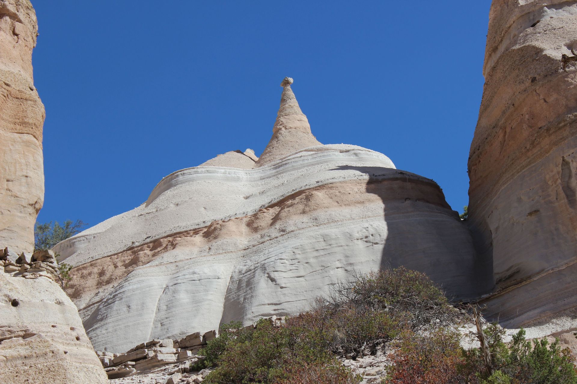 Cone-shaped tent rock formations rising under a clear blue sky in rural New Mexico.