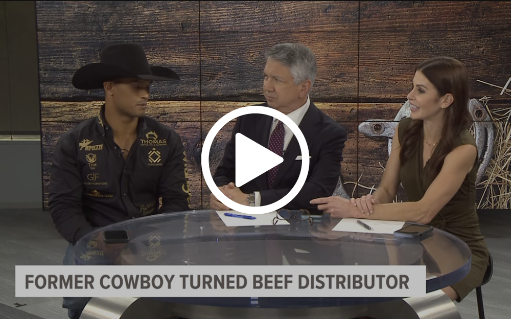 A former cowboy in a hat is interviewed at a table with two news anchors in a studio setting.