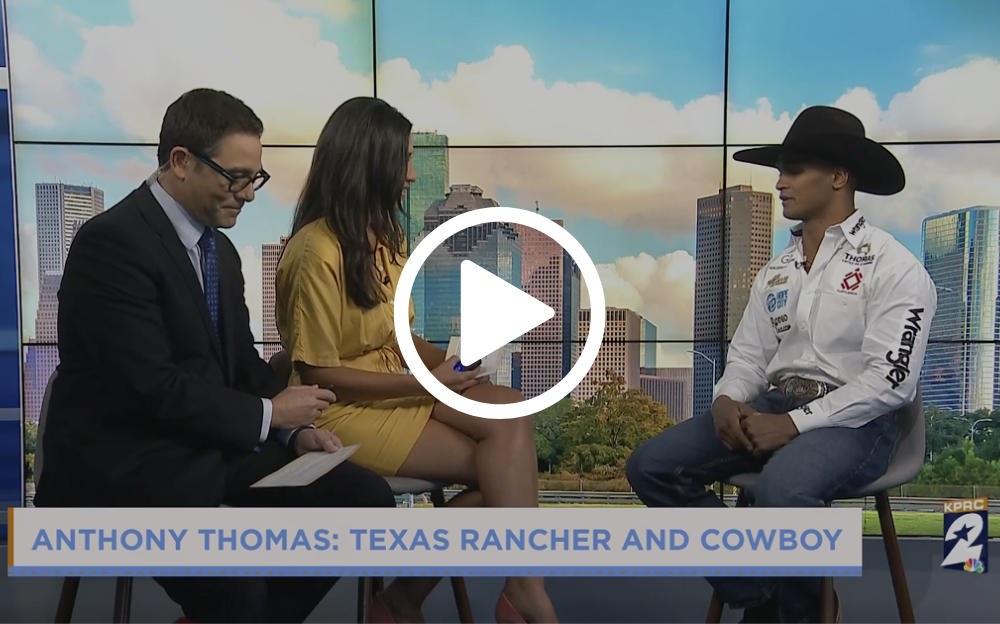 News anchors interview a cowboy wearing a hat and Western shirt; background city skyline.