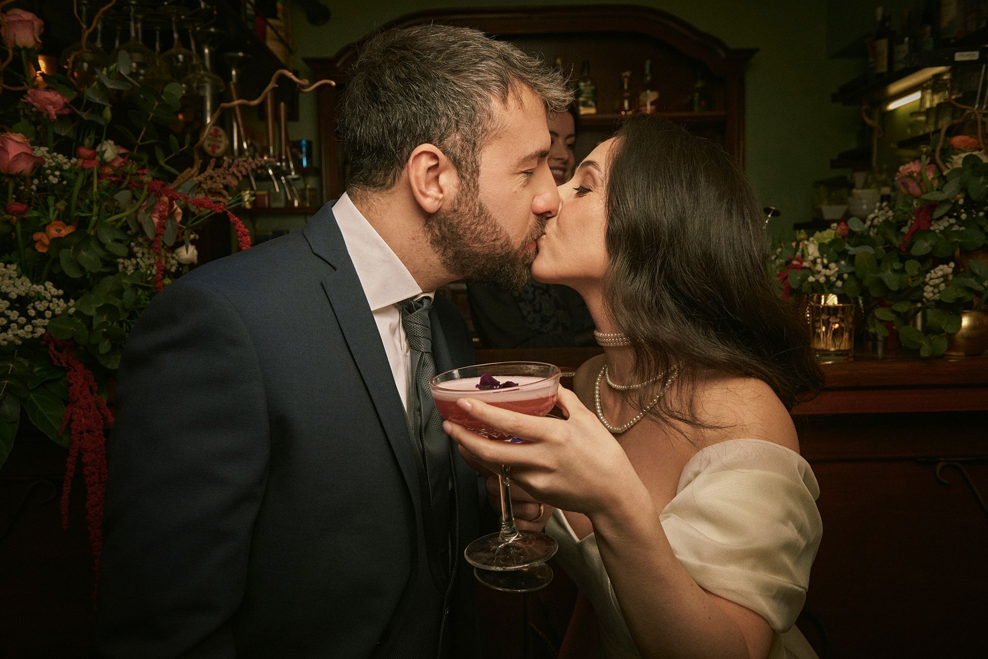 A man and a woman kiss while holding a drink