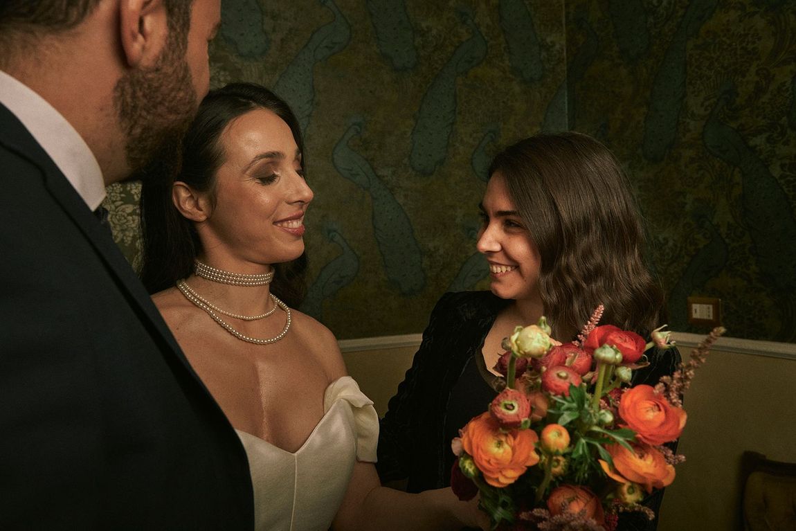 Una sposa e uno sposo stanno parlando con una donna che tiene in mano un mazzo di fiori.