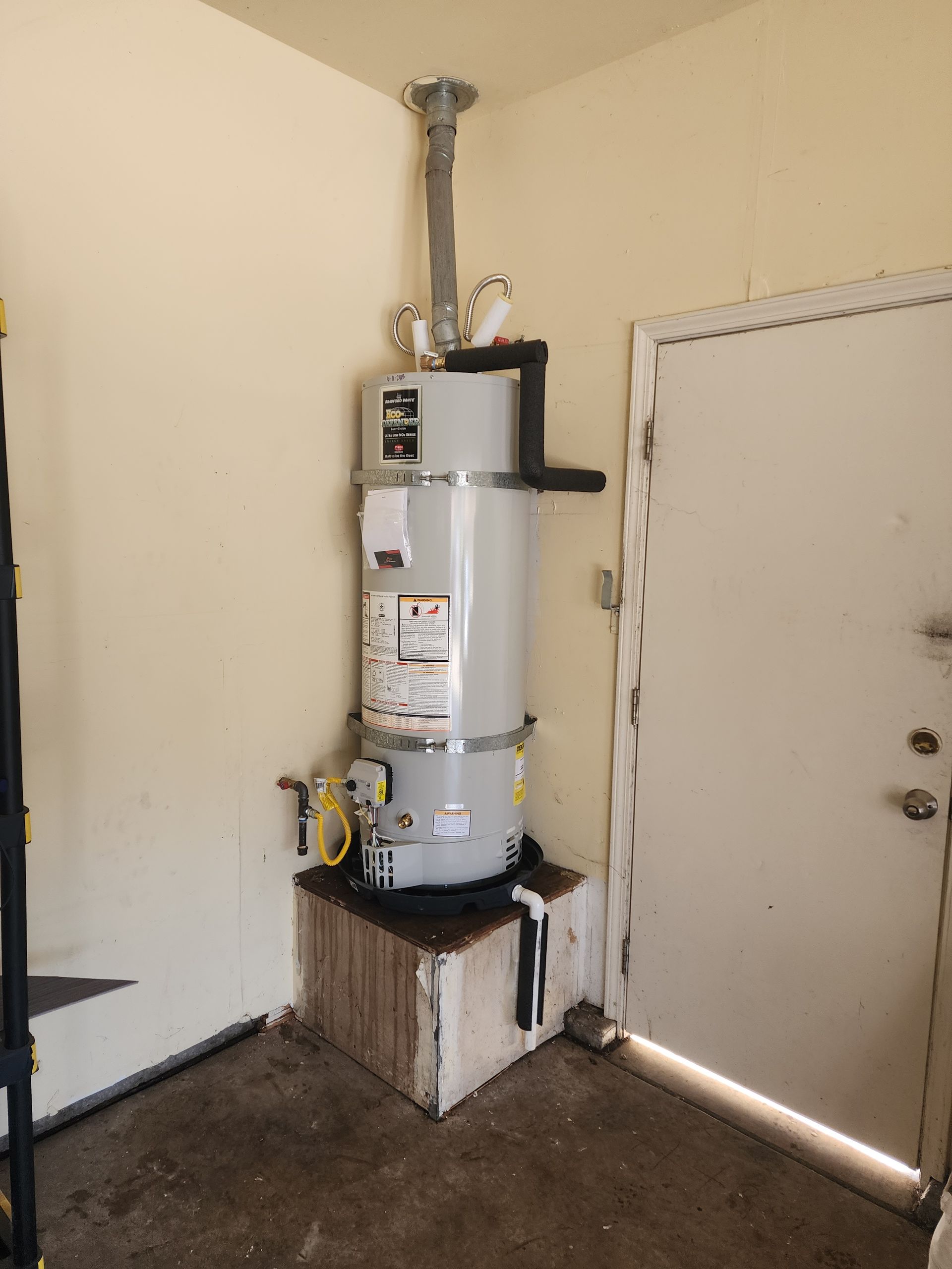 A water heater is sitting in a corner of a room next to a door