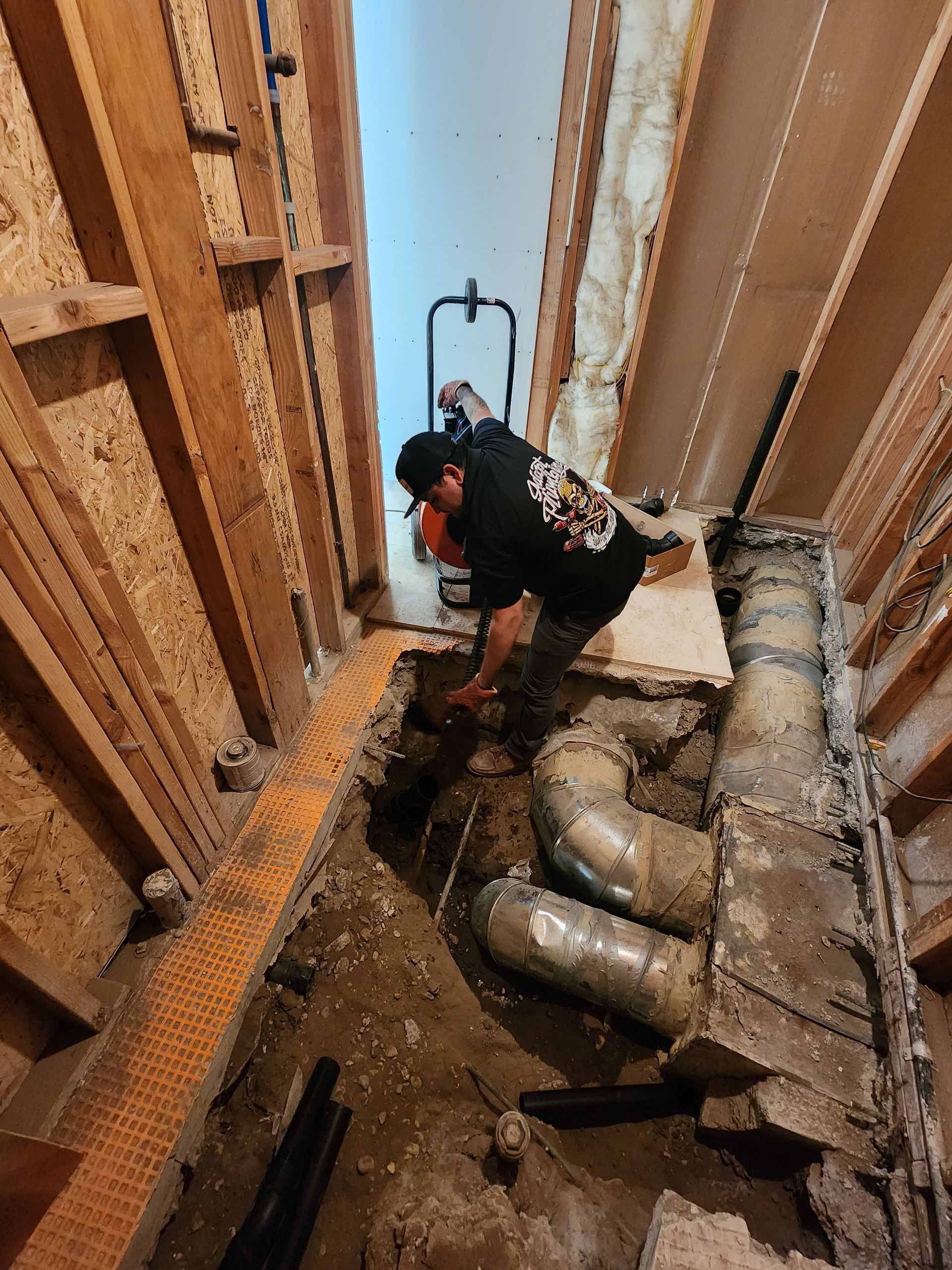 A man in a black shirt with a skull on the back is working on a pipe
