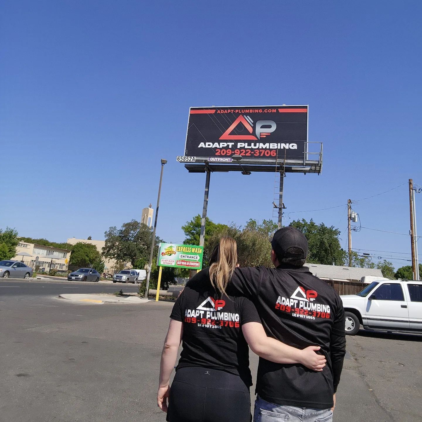 Two people standing in front of a billboard for ap plumbing