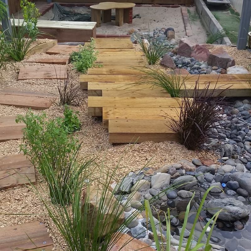 A Wooden Walkway Surrounded by Rocks and Plants in a Garden — Garden Vogue in Charlestown, NSW