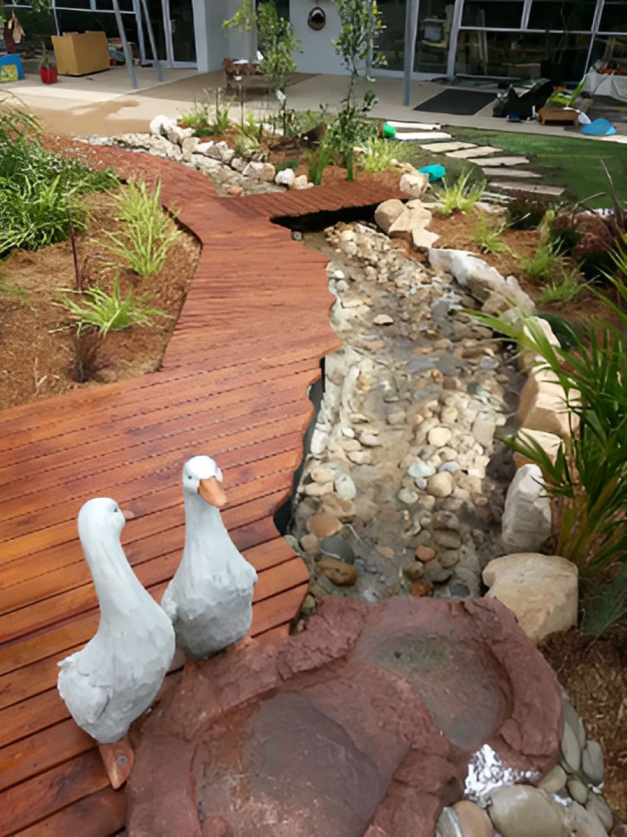 Three Ducks Are Standing on a Wooden Deck Next to a Stream — Garden Vogue in Charlestown, NSW