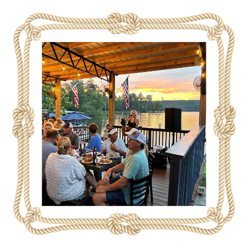 A group of people are sitting at tables on a patio overlooking a lake.
