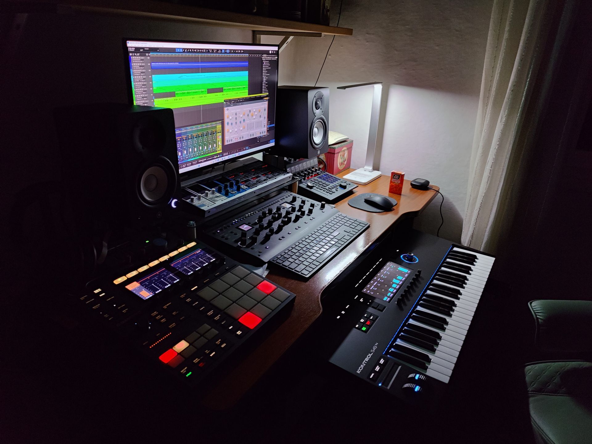 Music production studio with computer, keyboard, drum machine, speakers, and a midi keyboard.